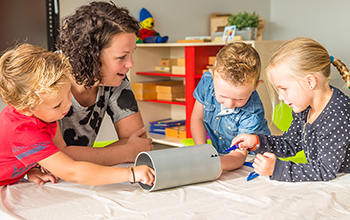 3 kids decorating a paper cylinder while adult watches