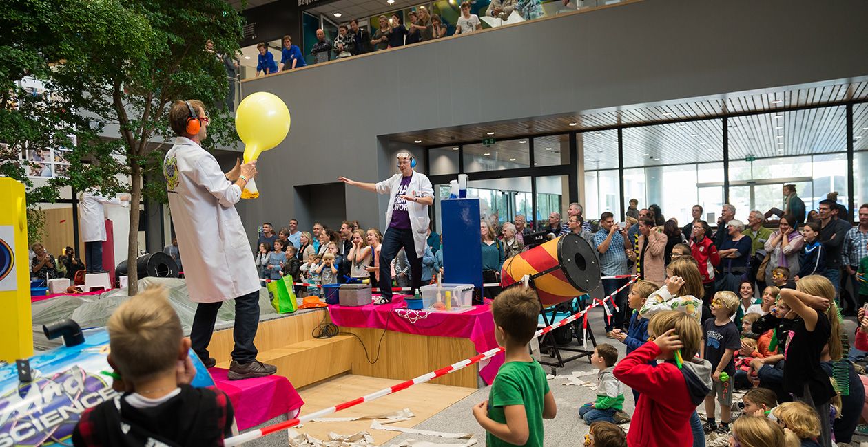 2 mad scientist on stage in front of a group of kids one holding a yellow balloon