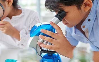 A boy looking through a microscope and a girl looking through a magnifying glass