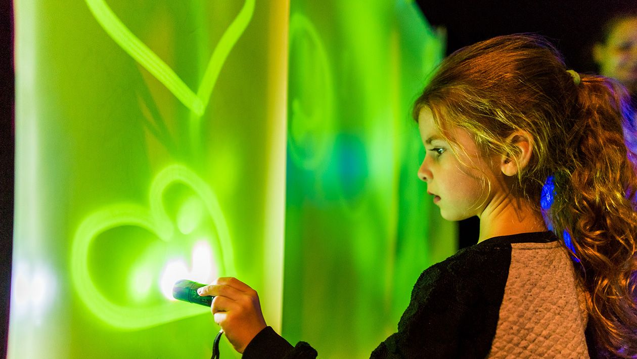 Girl with flashlight drawing on green lit up wall