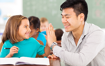 Girl high fiving teacher in the classroom while working on school work