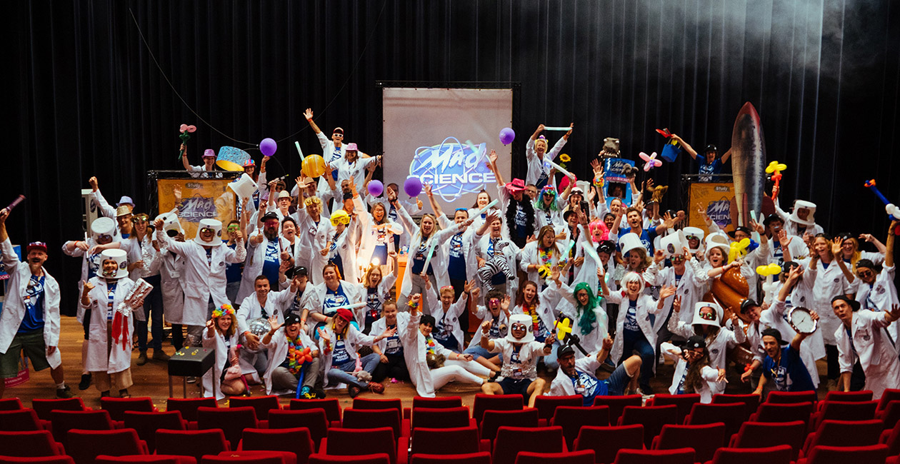 Mad Scientist on stage all wearing mad science lab coats with hands in the air wearing and holding different props