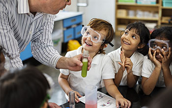 4 kids looking at teacher while he holds a test tube with a green substance inside