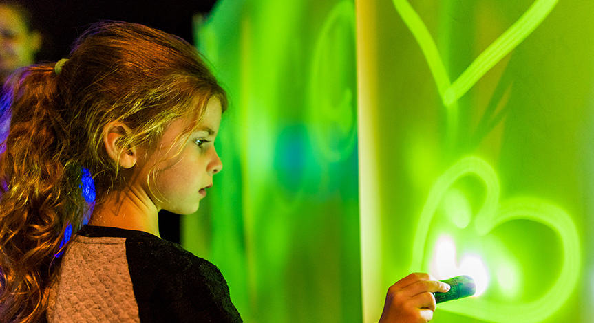 Girl with flashlight drawing on green lit up wall