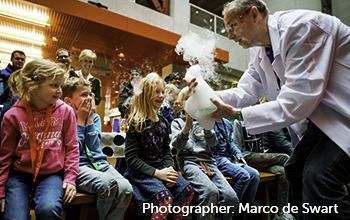Mad scientist showing a beaker with smoke and bubble poring out to children while parents look on