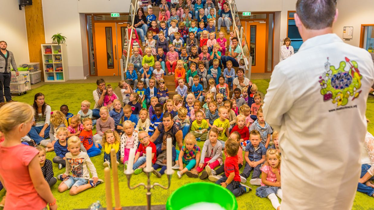 Mad scientist performing in front of kids sitting on the floor and up the stairs
