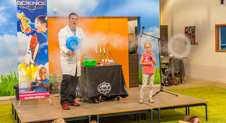 Mad scientist using smoke machine that is blowing rings while girl on stage looks on