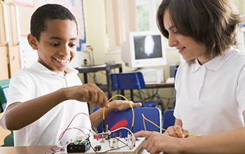 Boy and girl playing with wires attached to circuit board on a desk