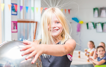 Blonde girl touching plasma ball causing her hair to stand in the air