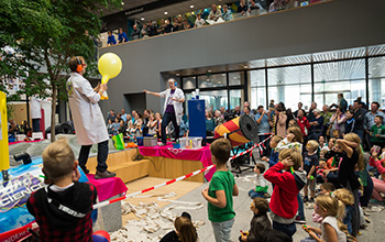 2 mad Scientist on stage in front of a group of kids one holding a yellow balloon
