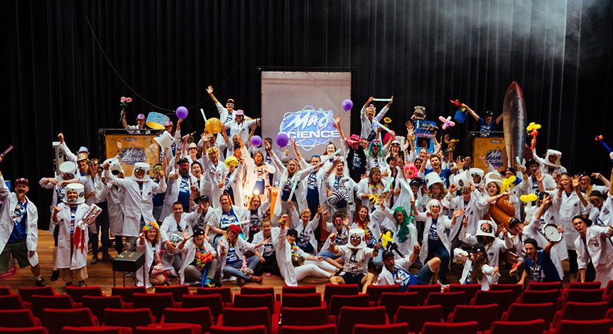 Mad Scientist on stage all wearing mad science lab coats with hands in the air wearing and holding different props