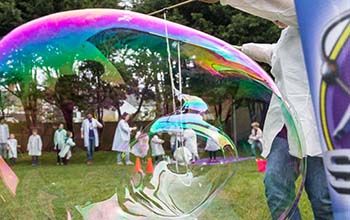 A kid in a mad science lab coat making a large bubble on grass